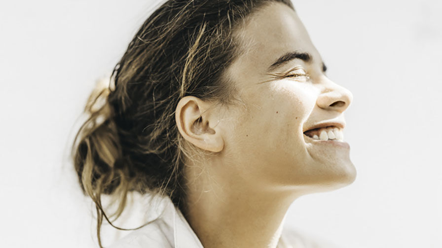 Mulher de olhos fechados e a sorrir, representando o impacto da menopausa na saúde oral