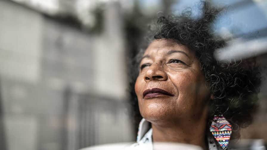 Mulher na menopausa a olhar pela janela com ar sereno  