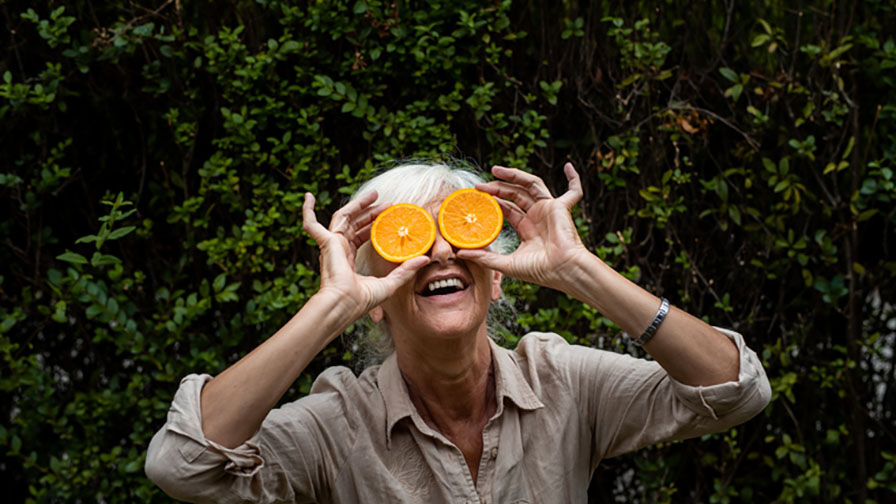 Mulher a segurar duas metades de laranja em frente aos olhos, representando cuidados com a saúde ocular na menopausa 